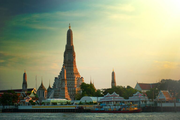 Wat Arun temple glowing at golden hour beside the Chao Phraya River in Bangkok, Thailand