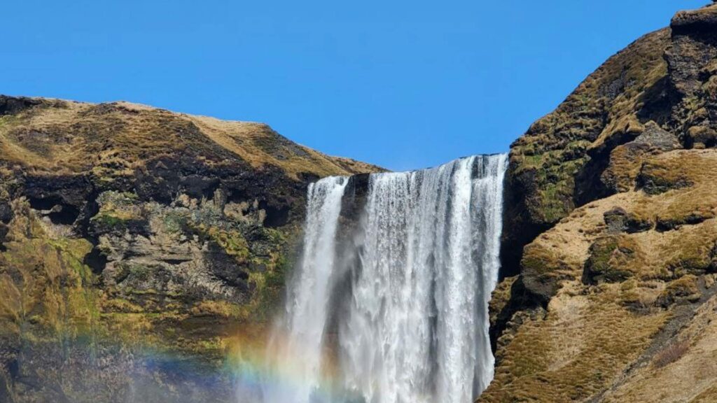Skogafoss waterfall with vibrant rainbow and visitors at the spray base, Iceland (1920px)
