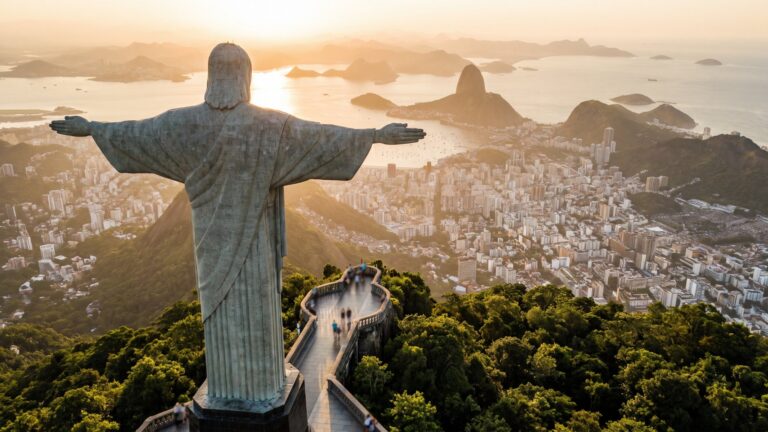 Christ the Redeemer on Corcovado at golden hour, with Sugarloaf Mountain, Guanabara Bay and the beaches of Rio de Janeiro spread out below