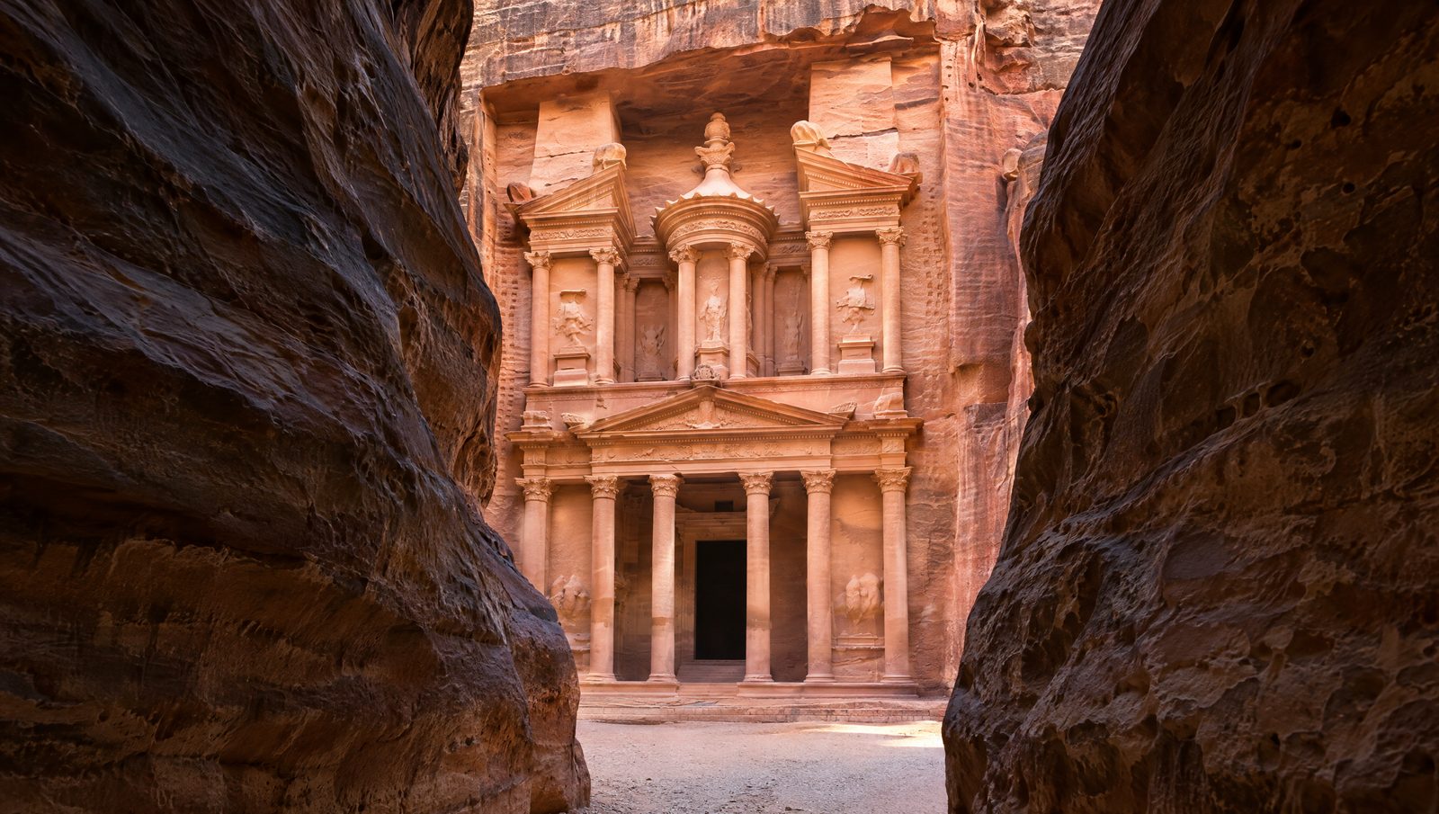 The rose-pink carved facade of Al-Khazneh, the Treasury at Petra, framed by the dark walls of the Siq