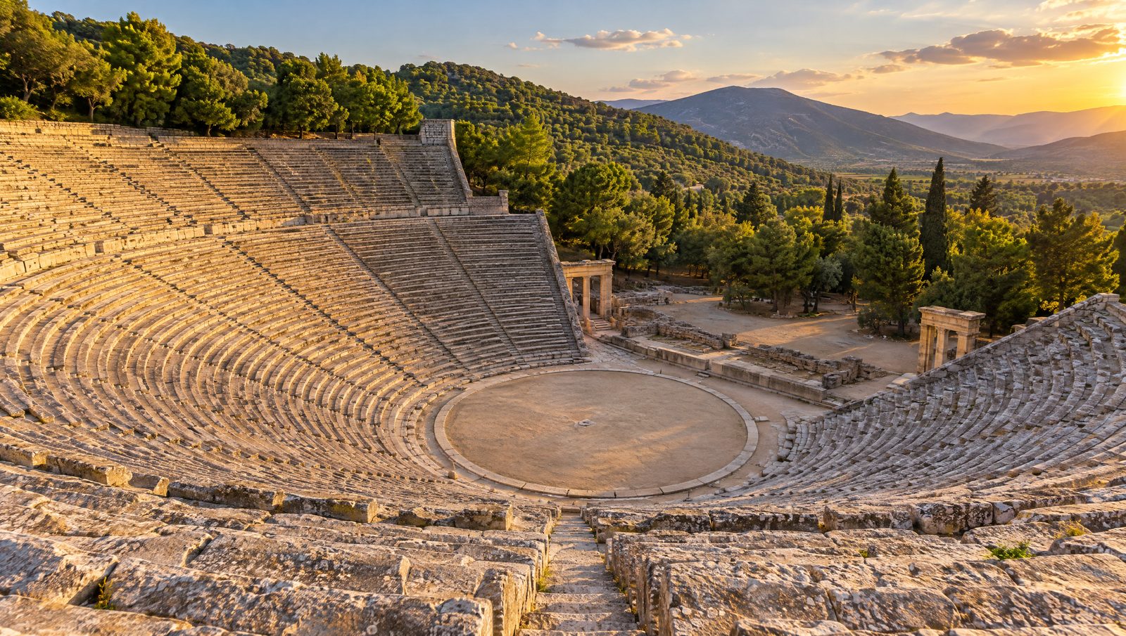 The limestone seating of the ancient theatre of Epidaurus rising in a semicircle around the orchestra, with pine hills behind