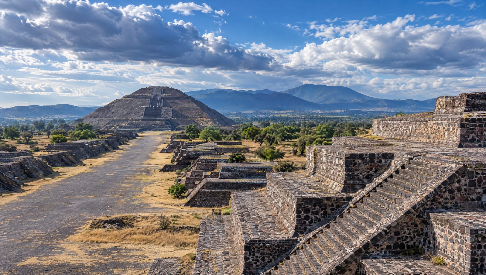 The Pyramid of the Sun at Teotihuacan seen along the Avenue of the Dead with stepped platforms in the foreground under dramatic clouds