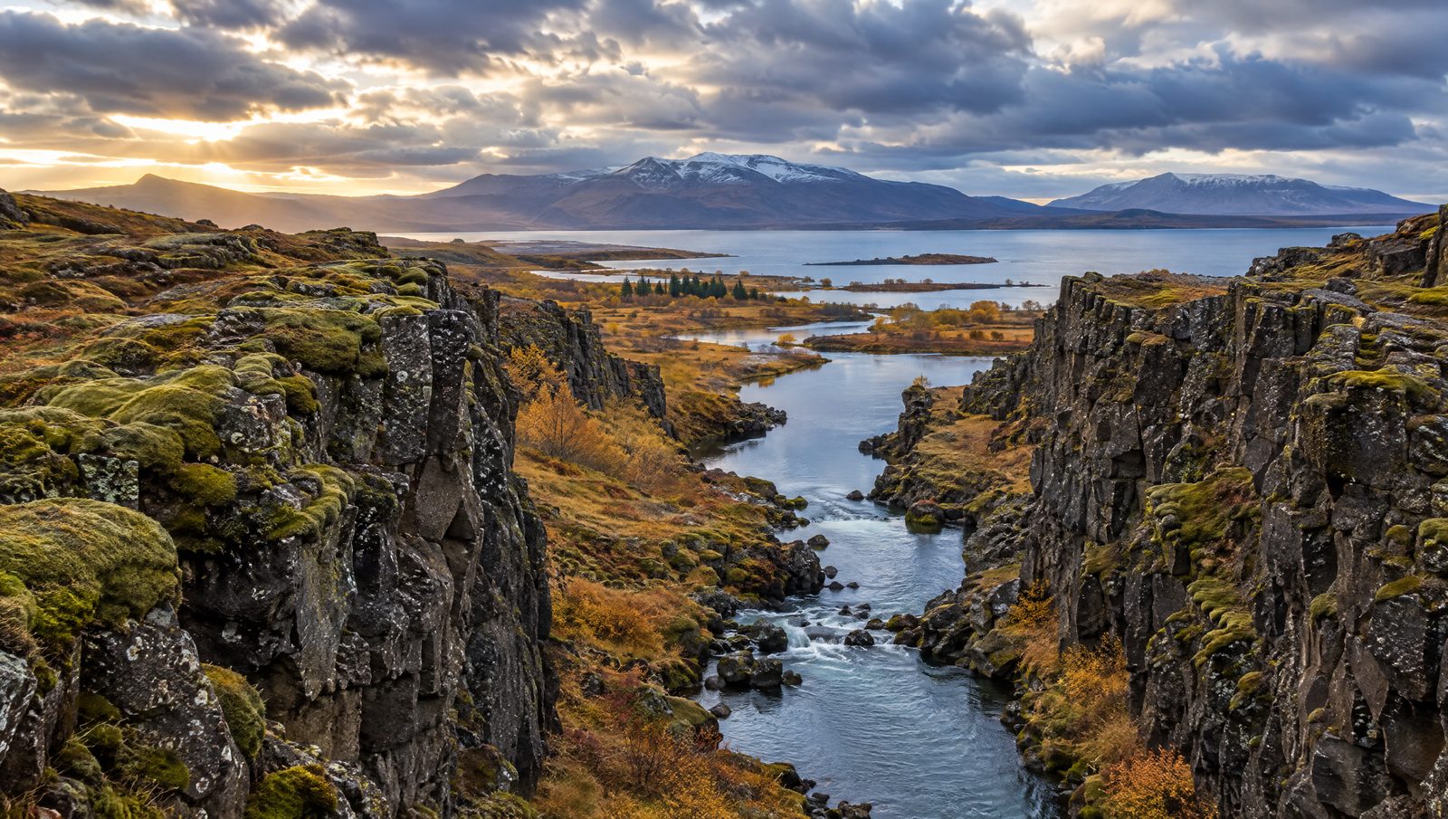 The Almannagjá rift at Þingvellir, Iceland, with dark basalt walls, the Öxará river and lake Þingvallavatn beyond